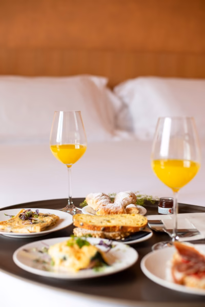 Frühstückstablett beim Zimmerservice in einem Hotelzimmer - im Hintergrund ist das weisse Bett zu sehen